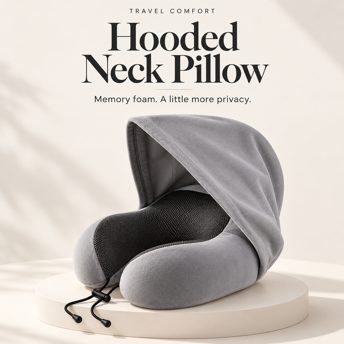 Light gray hooded memory foam travel neck pillow on an ivory studio pedestal